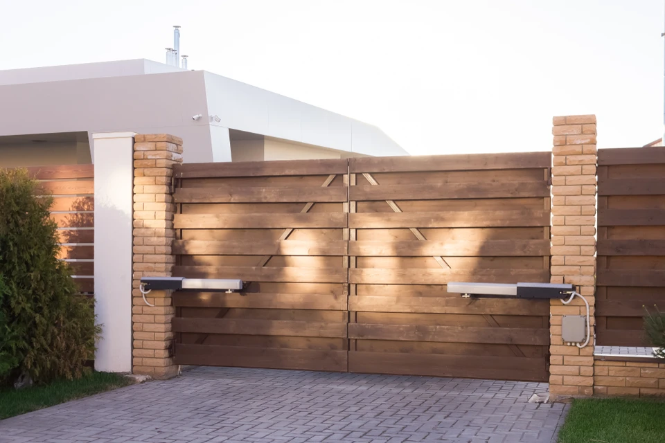 Portail automatique résidentiel en bois avec piliers maçonnés, installé devant une maison moderne