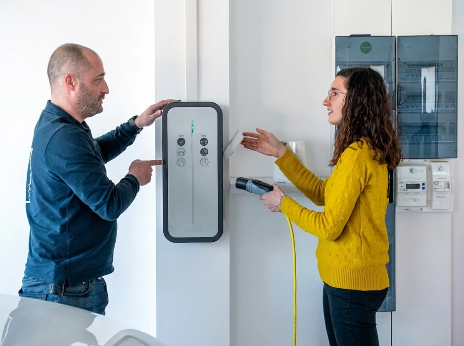 Deux personnes face à une borne de recharge pour véhicule électrique murale marque **Thegor**, installée en intérieur