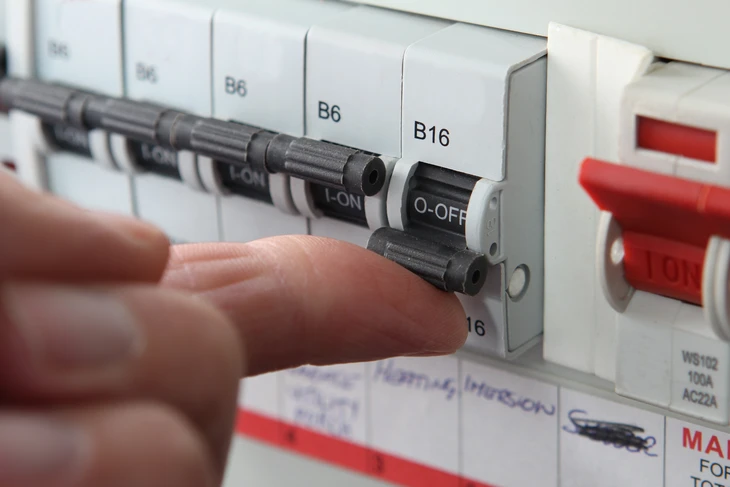 Électricien avec casque de protection bleu travaillant sur un tableau électrique industriel ouvert