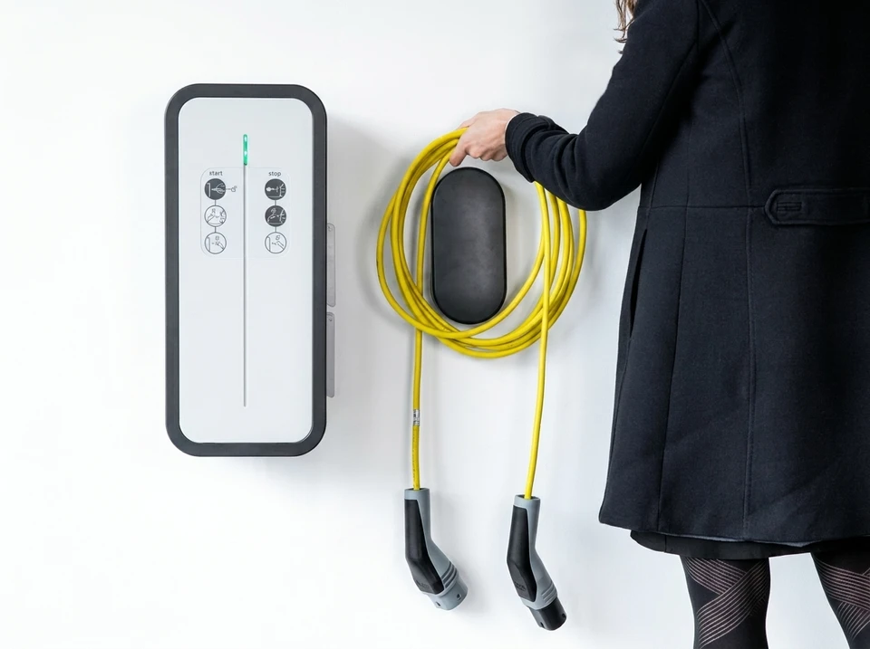Gros plan professionnel montrant un électricien en tenue de travail installant ou branchant une borne de recharge pour véhicules électriques sur un mur de bâtiment ou parking. La borne doit être clairement visible et bien définie. Le professionnel manipule les connecteurs ou les fils de connexion avec précision. L'arrière-plan doit montrer un environnement professionnel (parking, bâtiment commercial, ou résidence collective). Lumière naturelle ou éclairage professionnel de chantier.